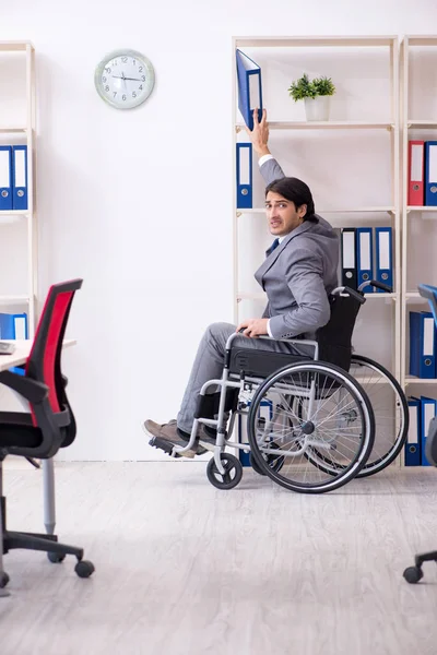 Young handsome employee in wheelchair working in the office