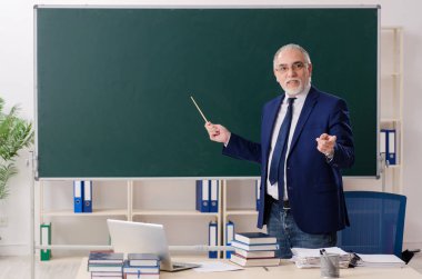 Tahtanın önünde yaşlı bir erkek öğretmen. 