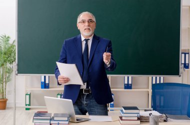 Tahtanın önünde yaşlı bir erkek öğretmen. 