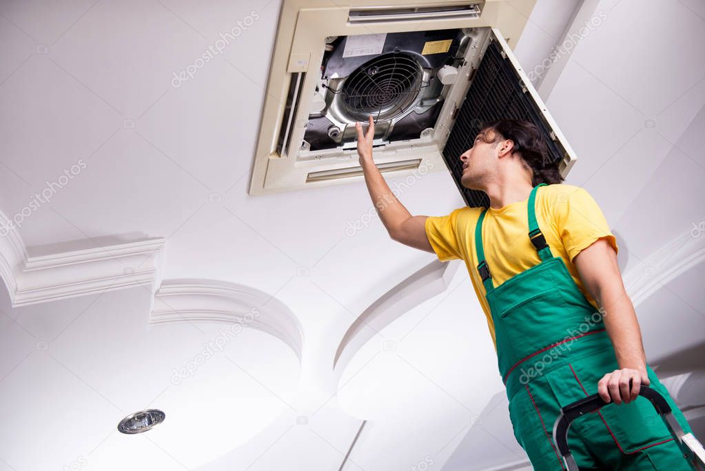 Young repairman repairing ceiling air conditioning unit 