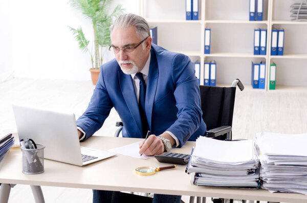 Пожилой работник в инвалидной коляске работает в офисе
 