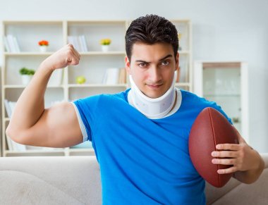 Boynu yaralanmış bir adam evde Amerikan futbolu seyrediyor.
