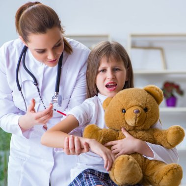 Kadın doktor oyuncak ayıyla küçük tatlı kızı muayene ediyor.