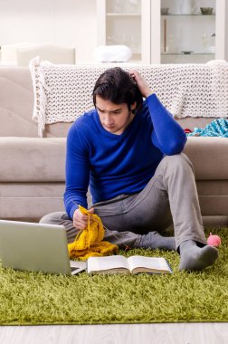 Genç yakışıklı adam evde örgü örüyor.