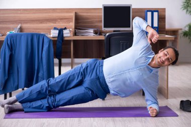 Genç yakışıklı işadamı iş yerinde egzersiz yapıyor. 