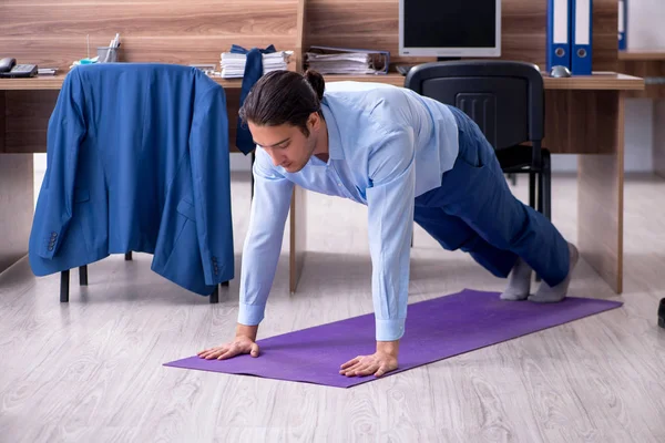Young handsome businessman doing exercises at workplace — Stock Photo, Image