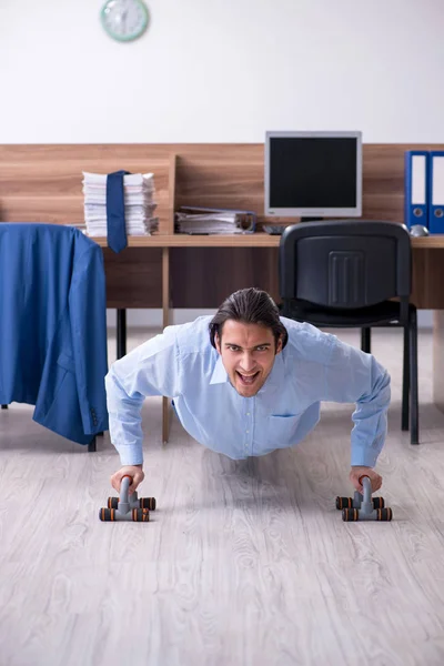 Young handsome businessman doing exercises at workplace — Stock Photo, Image