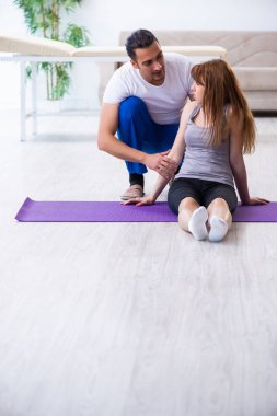 Erkek fizyoterapist yerde yaralı bir kadınla egzersiz yapıyor.