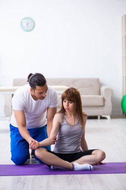 Erkek fizyoterapist yerde yaralı bir kadınla egzersiz yapıyor.