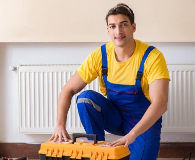 Genç tamirci müteahhit ısıtma panelini tamir ediyor.