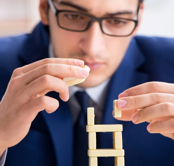 Young businessman building domino tower in office — Stock Photo, Image