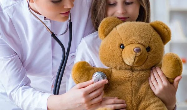 Kadın doktor oyuncak ayıyla küçük tatlı kızı muayene ediyor. — Stok fotoğraf