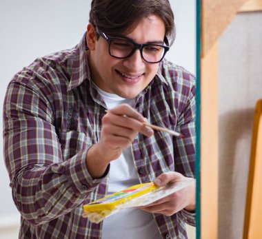 Genç erkek sanatçı parlak stüdyoda resimler çiziyor.