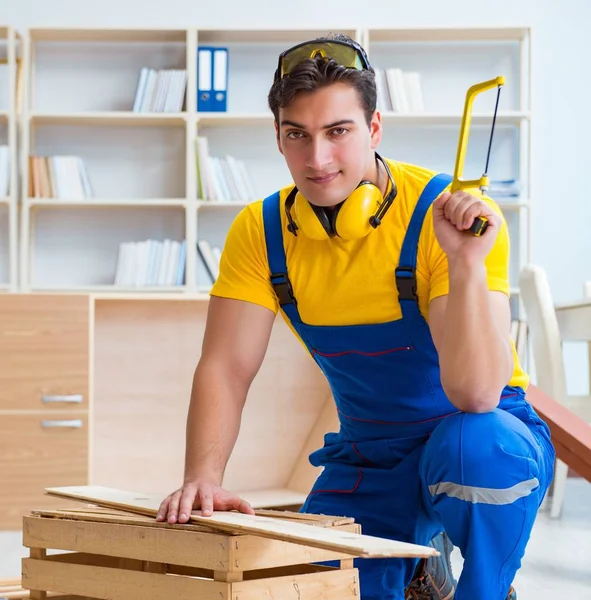 Reparador carpintero trabajando aserrando una tabla de madera con una mano sa — Foto de Stock