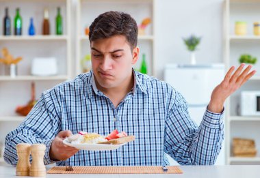 Genç koca öğle yemeğinde tatsız yemekler yiyor.