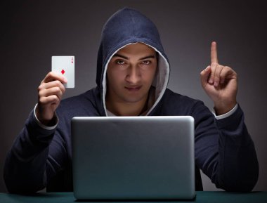 Kapüşonlu genç adam dizüstü bilgisayarın önünde oturuyor.