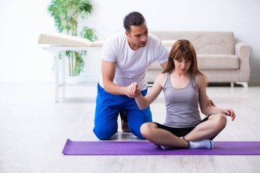 Erkek fizyoterapist yerde yaralı bir kadınla egzersiz yapıyor.