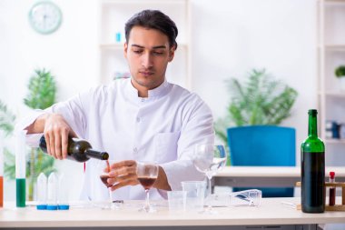 Erkek kimyager laboratuvarda şarap örneklerini inceliyor.