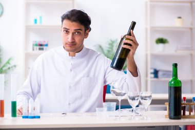 Erkek kimyager laboratuvarda şarap örneklerini inceliyor.