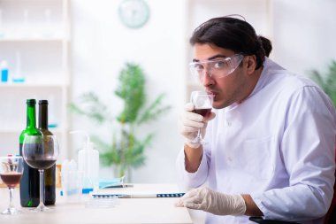 Erkek kimyager laboratuvarda şarap örneklerini inceliyor.