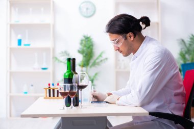 Erkek kimyager laboratuvarda şarap örneklerini inceliyor.