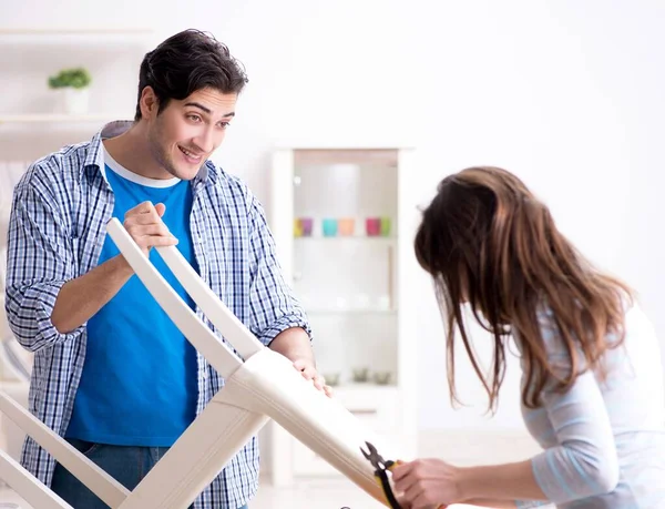 Жена помогает мужу починить сломанное кресло дома — стоковое фото