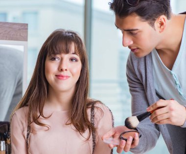 Güzellik salonunda güzel bir kadın için makyaj yapan adam.