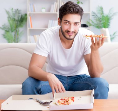 Pizza yiyen adam evde yemek yiyor, dinleniyor.