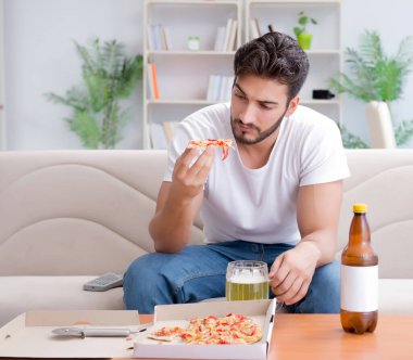 Pizza yiyen adam evde yemek yiyor, dinleniyor.