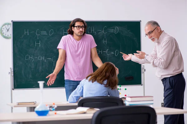 Old chemist teacher and two students in the classroom