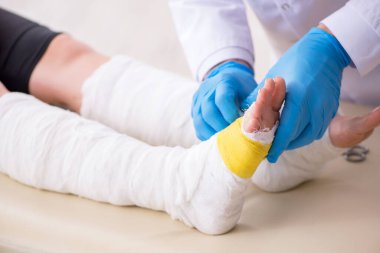 Genç bacak yaralı kadın yaşlı doktor travmatoloğu ziyaret ediyor.