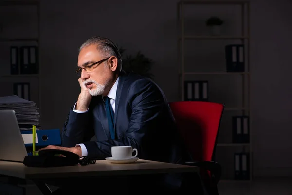 Old male employee working late at workplace