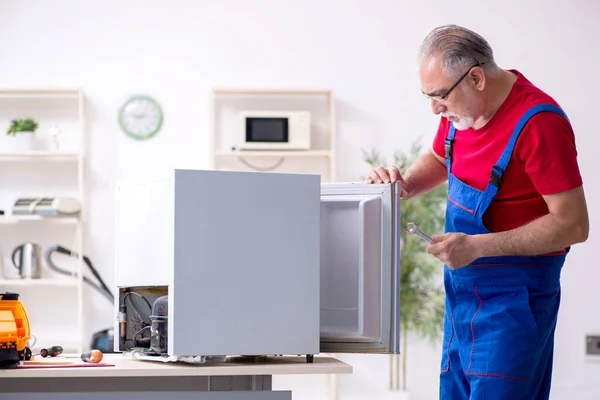 Velho empreiteiro masculino reparando geladeira dentro de casa — Fotografia de Stock