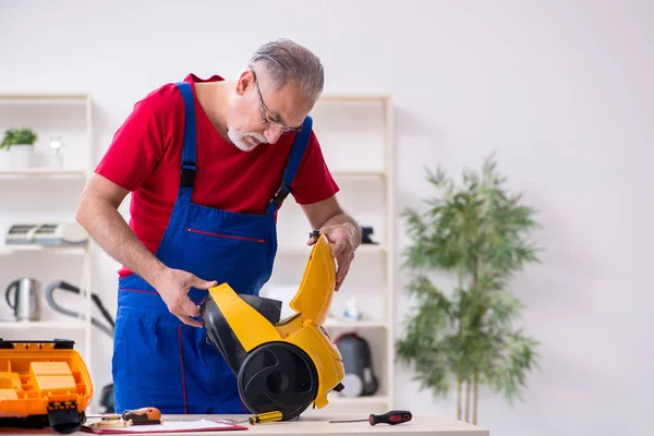 修理室内真空吸尘器的老男性承包商 — 图库照片
