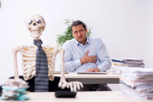 Ung manlig anställd och skelett på kontoret — Stockfoto