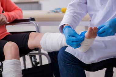 Genç bacak yaralı kadın yaşlı doktor travmatoloğu ziyaret ediyor.