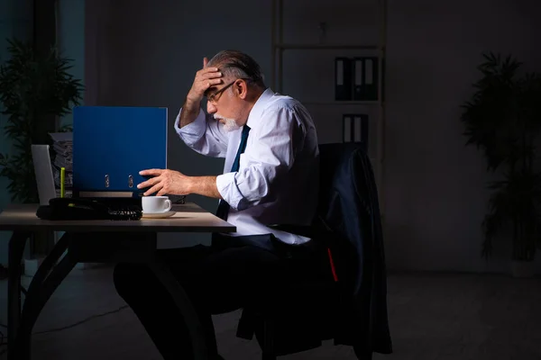 Old male employee working late at workplace