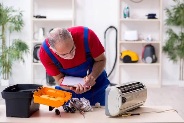 Antigo empreiteiro masculino reparando ar ar condicionado dentro de casa — Fotografia de Stock