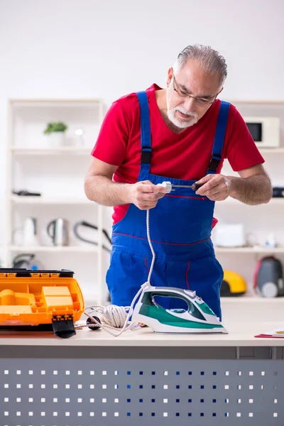 Velho empreiteiro masculino reparando ferro dentro de casa — Fotografia de Stock