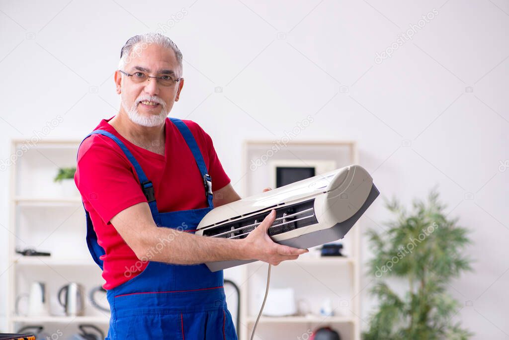 Old male contractor repairing air-conditioner indoors