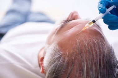 Yaşlı adam saç nakli için genç erkek doktoru ziyaret ediyor.