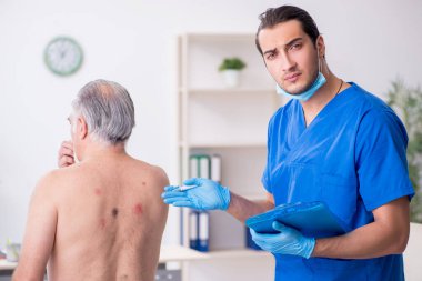 Yaşlı adam genç erkek doktor dermatoloğu ziyaret ediyor.