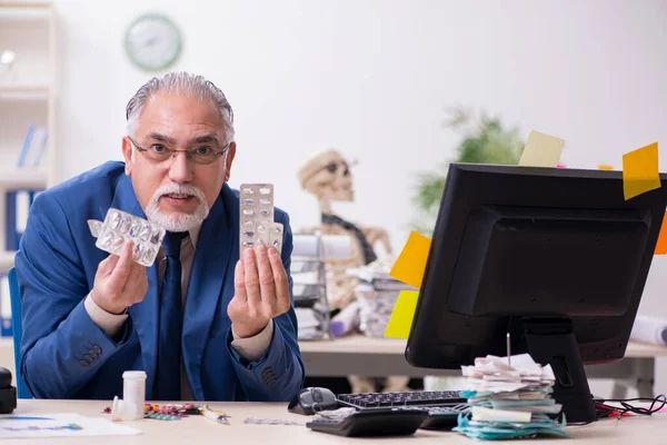 Old male sick employee working overtime in the office