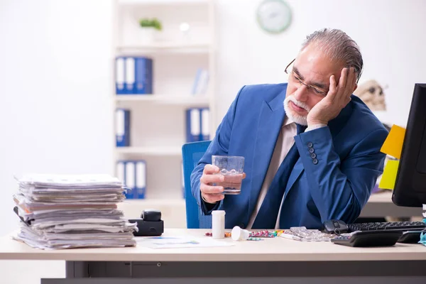 Starý muž nemocný zaměstnanec pracující přesčas v kanceláři — Stock fotografie