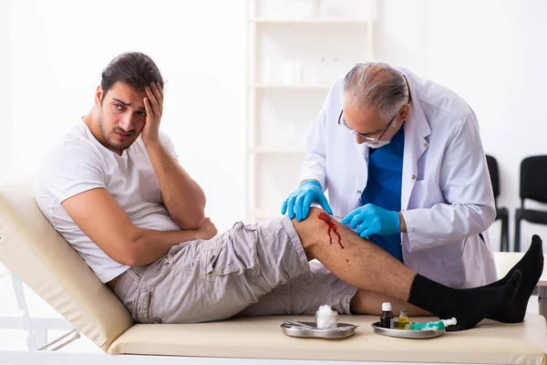 Leg injured man visiting old doctor in first aid concept — Stock Photo, Image