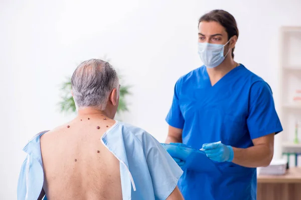 Homem velho visitando jovem médico dermatologista masculino — Fotografia de Stock