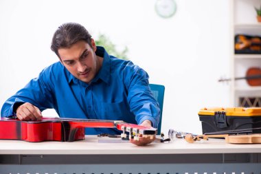 Gitarı tamir eden genç bir erkek tamirci.