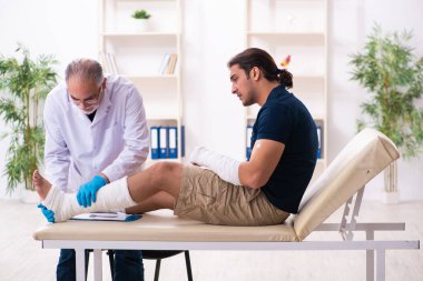 Genç yaralı adam yaşlı doktor travmatoloğu ziyaret ediyor.