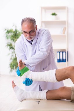 Genç yaralı adam yaşlı doktor travmatoloğu ziyaret ediyor.