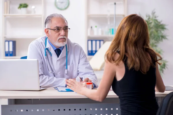 Jovem mulher visitando velho médico masculino — Fotografia de Stock